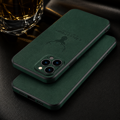Two green textured cases overlap on a dark surface beside a glass, showing camera openings and embossed deer designs.