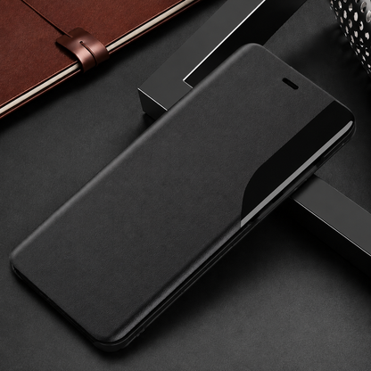 Closed black flip phone case lying on dark geometric blocks beside a brown notebook, with a curved glossy strip along its right edge.