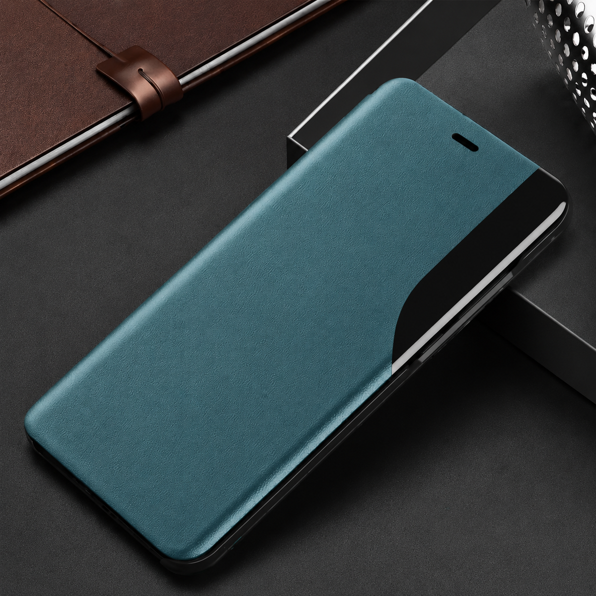 Teal flip phone case lying diagonally on dark blocks, with an earpiece slit and curved glossy black viewing strip along the right edge.