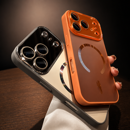 Hand holds orange and silver-gray cases together above a wooden table. Reflective magnetic rings decorate both backs, and their raised camera panels remain visible.