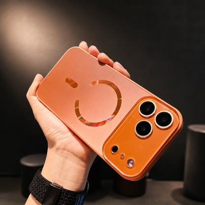 Hand wearing a black watch holds an orange case horizontally. Its reflective circular magnetic ring and alignment bar catch light beside the raised camera panel.