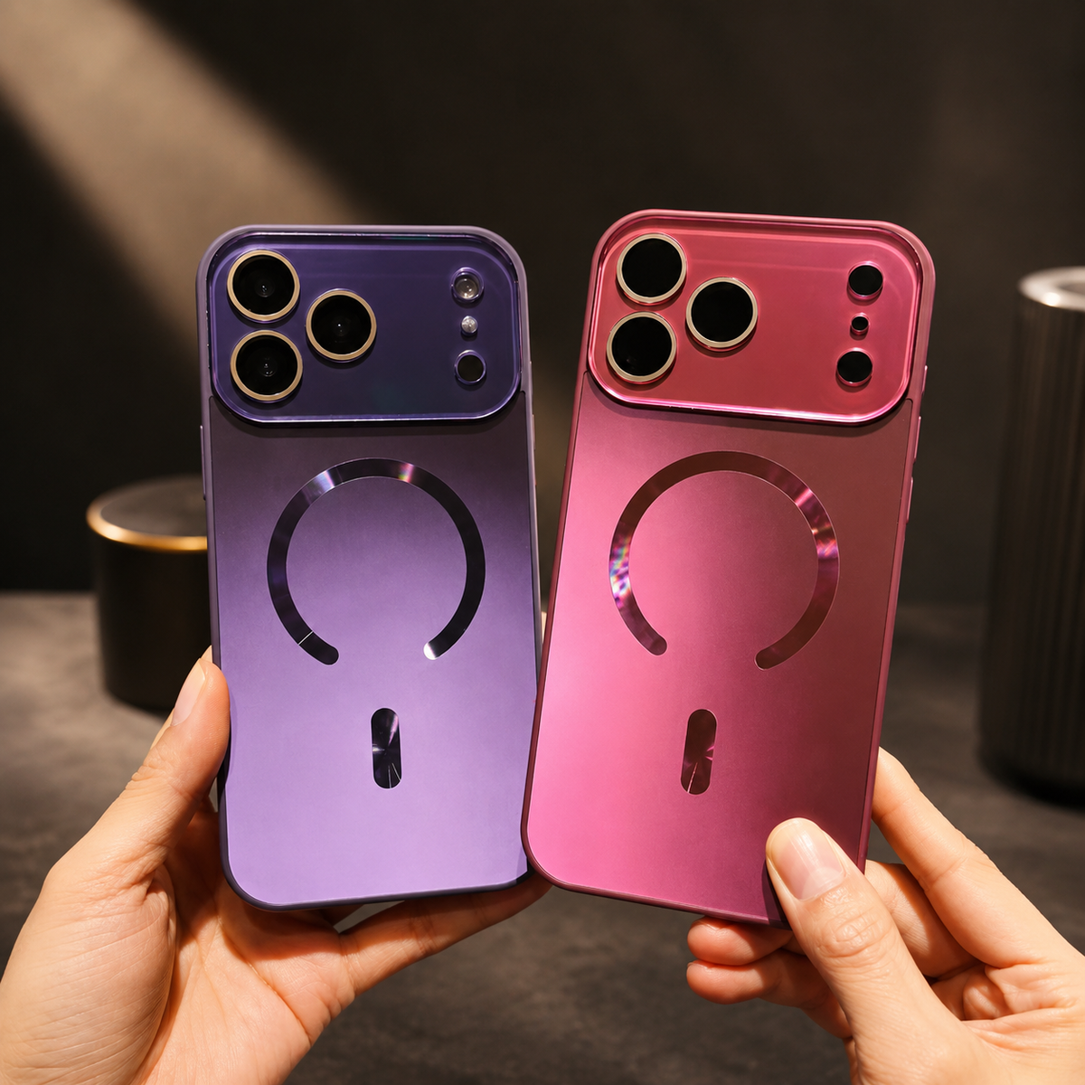 Hands hold purple and pink cases upright side by side. Both backs have reflective magnetic rings and broad matching camera panels with individually framed lenses.