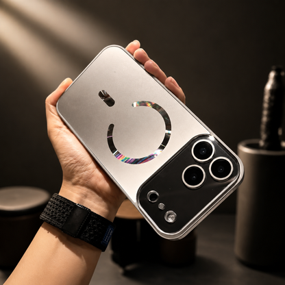 Hand wearing a black watch holds a silver-gray case horizontally. A reflective rainbow-tinted magnetic ring decorates the back beside a dark camera panel.