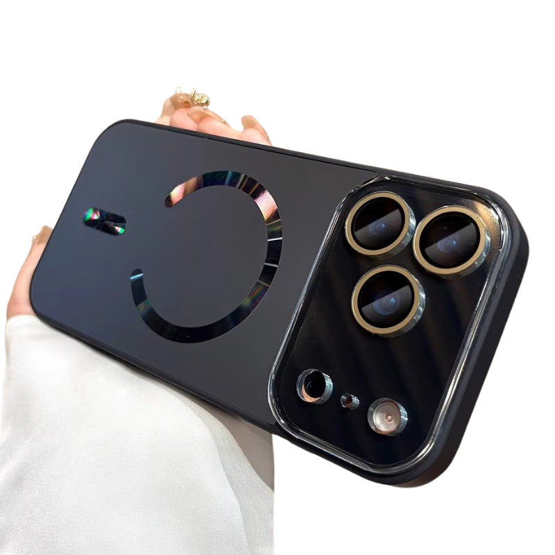 Hand holds a black case horizontally against white. A reflective rainbow-tinted magnetic ring and alignment bar decorate the back, with gold-colored rings around the camera lenses.