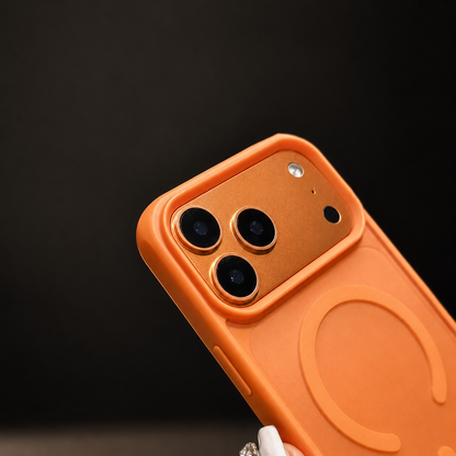 A hand holds an orange case diagonally against black, showing its camera opening and circular magnetic design.