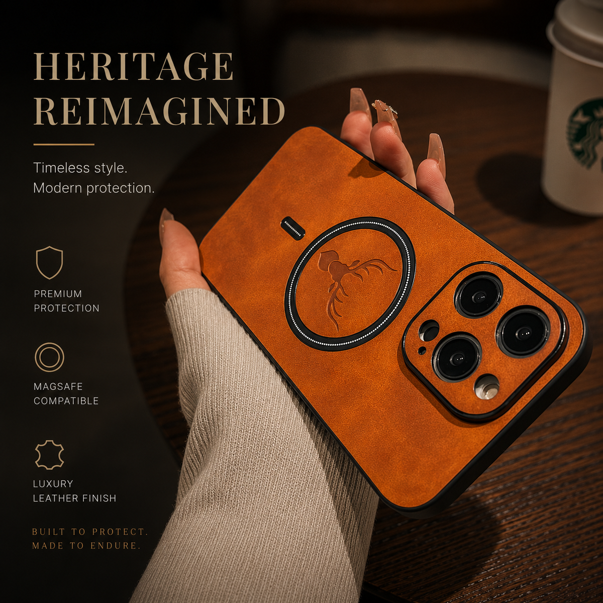 A hand in a cream knit sleeve holds an orange-tan stag-emblem phone case diagonally above a wooden café table. A takeaway cup is partly visible behind it. Dark raised camera borders, a circular magnetic ring and short alignment mark stand out on the back. The heading reads Heritage Reimagined.