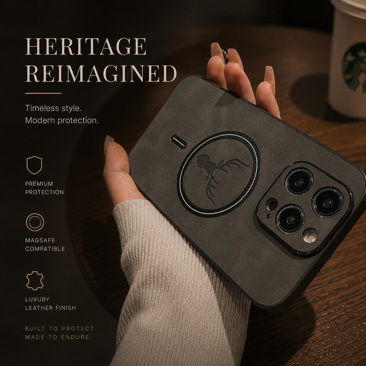 A hand in a cream knit sleeve holds a charcoal stag-emblem case diagonally above a wooden café table. Its dark magnetic circle, deer head and raised camera surround are visible beside a blurred takeaway cup. The heading reads Heritage Reimagined.