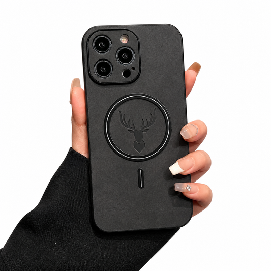 A hand emerging from a black sleeve holds a charcoal phone case upright on white. The soft-looking mottled back has a black circular magnetic ring around an embossed stag head, with a short vertical mark below. Raised dark borders surround the camera lenses at the upper left.