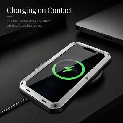 A silver rugged phone lies screen-up on a dark desk with a green charging indicator. Text advertises charging through the case.