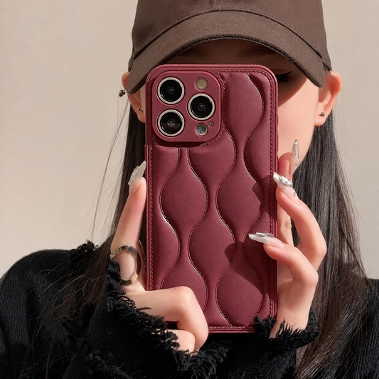 A woman in a brown cap holds a burgundy case in front of her face, showing rounded padded-looking waves and stitched edges.