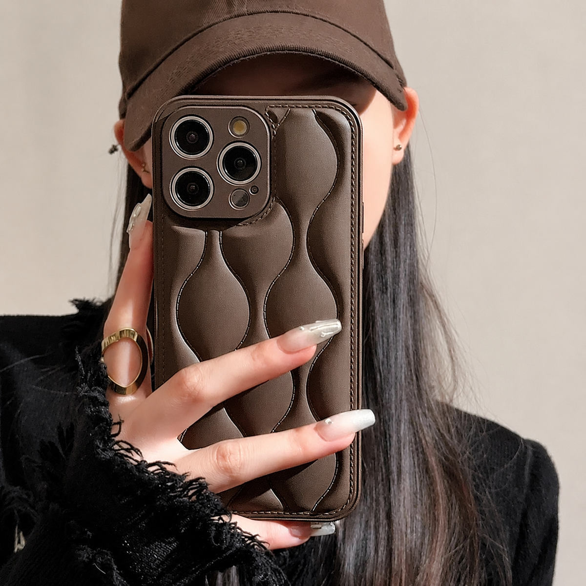 A woman in a brown cap holds a brown case with stitched, raised wavy sections on its back.