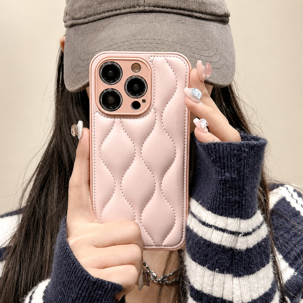 A woman in a gray cap and striped sweater holds a pale pink case with stitched, padded-looking wavy sections.