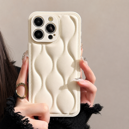 A hand holds a cream case upright, showing three camera lenses and rounded raised sections formed by wavy stitching.