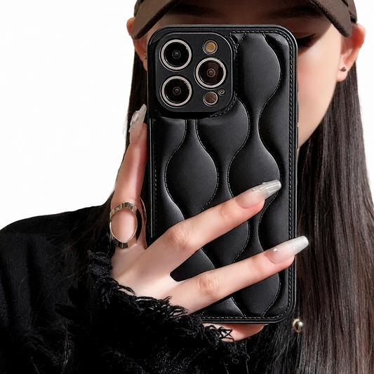 A woman in a brown cap holds a black case in front of her face. Its padded-looking back is divided by stitched wavy vertical seams into rounded raised sections.