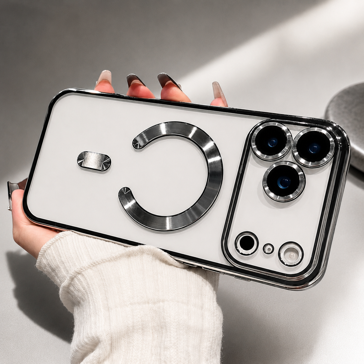 A hand holds a white phone horizontally in a silver-trimmed clear case, showing its shiny open circular ring and individual camera rims.