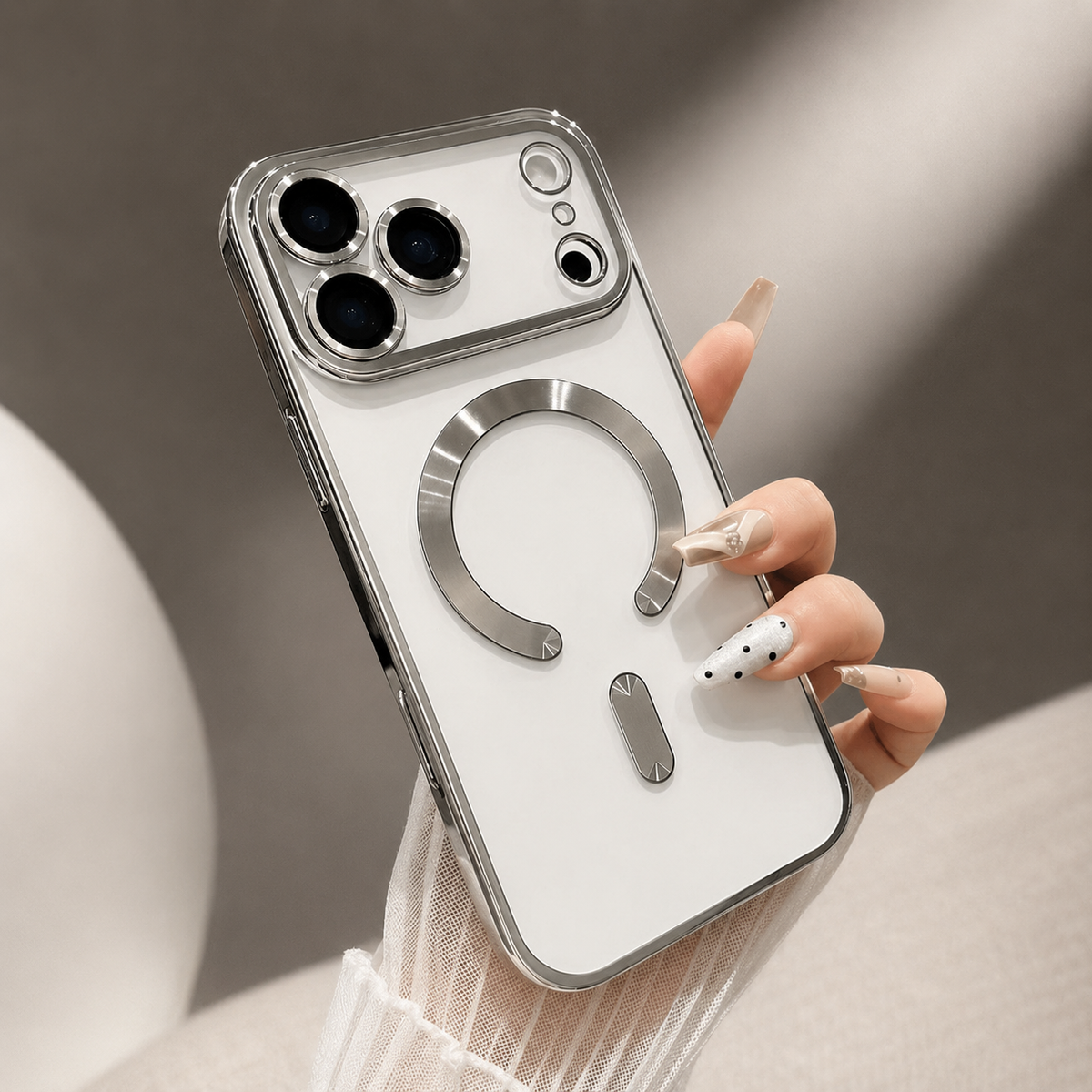 A hand holds a silver-trimmed clear case on a white phone, showing its individual camera rims and shiny horseshoe-shaped ring and bar.