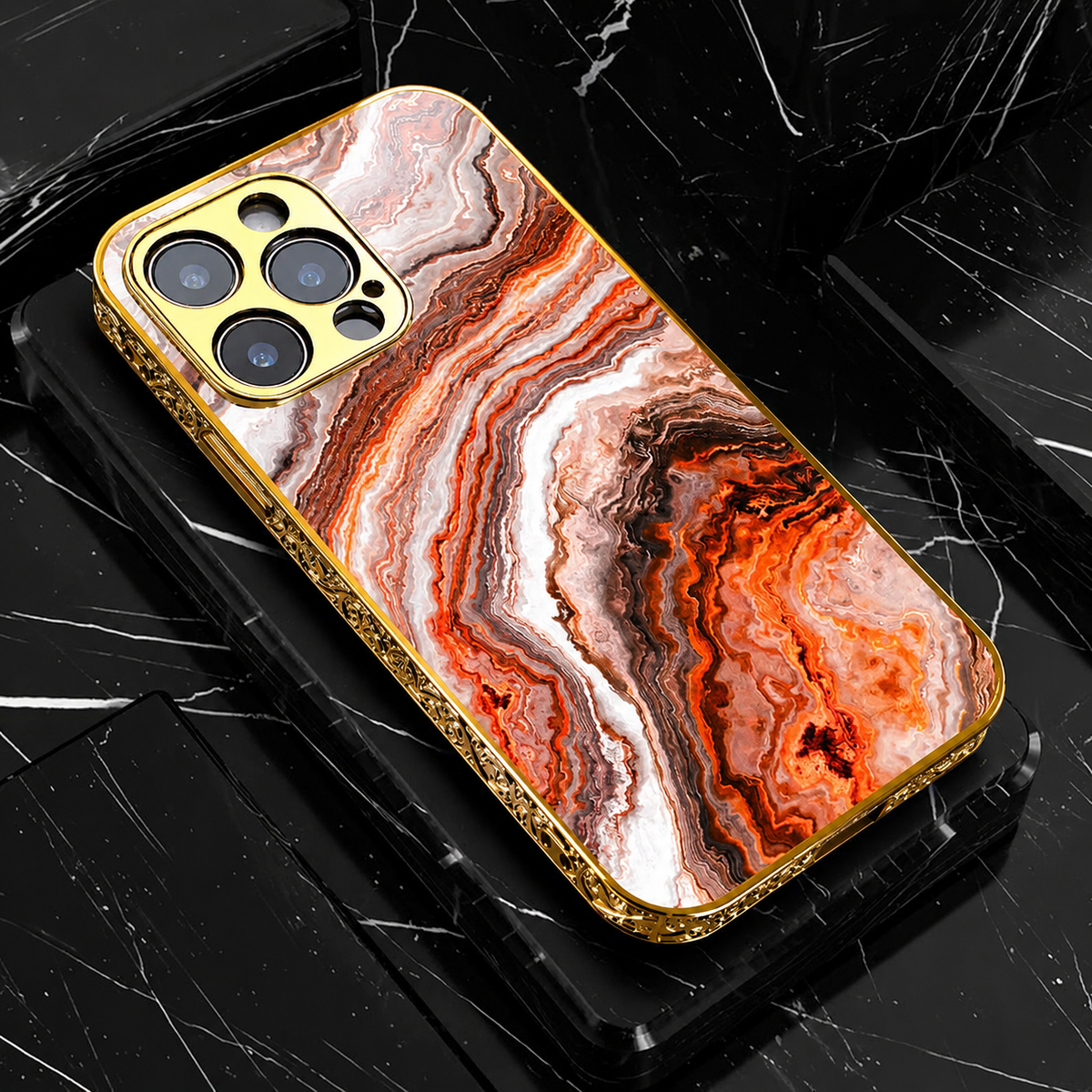 An orange, white and brown marble-pattern phone case lies on black blocks. Wavy bands cross its back inside ornate gold-colored edges and a matching camera surround.