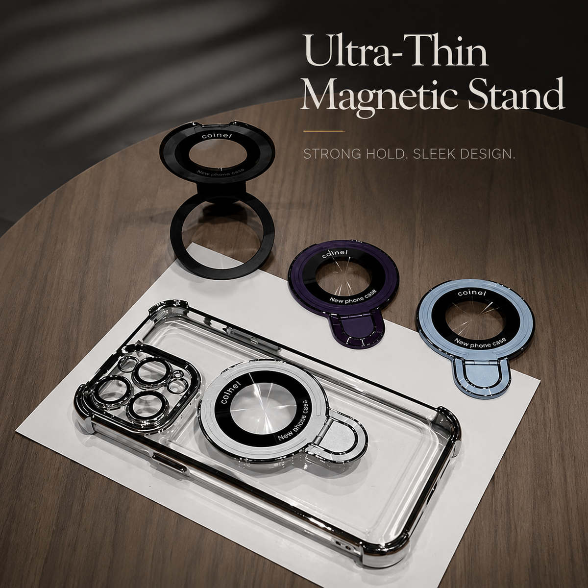 A clear phone case lies on white paper on wood, beneath separate black, purple and blue ring stands. Text advertises an ultra-thin magnetic stand and sleek design.