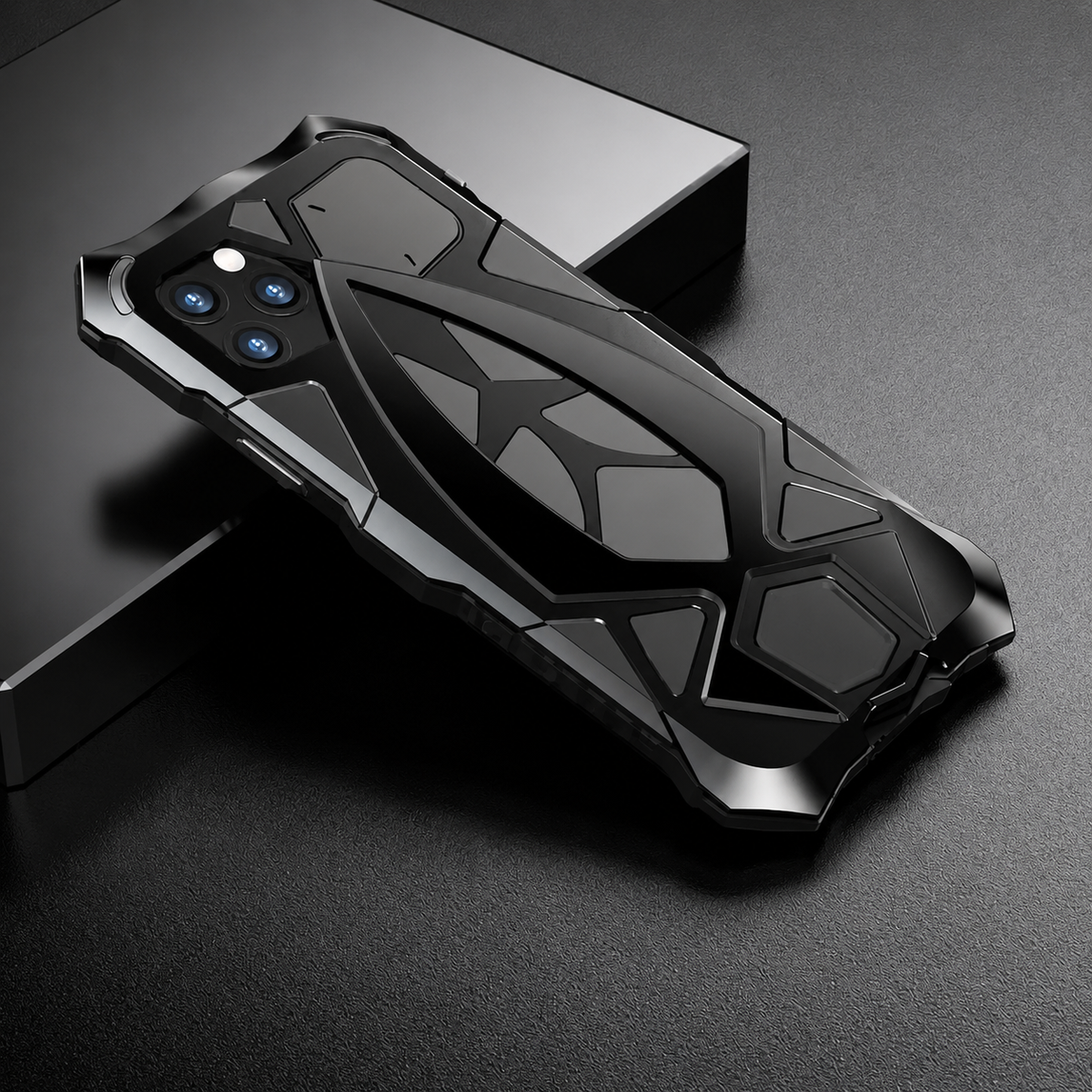 A black armor-style case rests diagonally across a dark display block, showing geometric rear layers and angular corner guards.