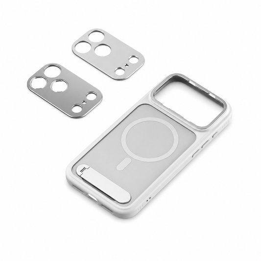An empty silver photography phone case lies diagonally on white beside two removable camera plates with circular lens openings. A circular magnetic marking and short alignment bar occupy the back, with a recessed folding stand near the bottom and a broad camera opening above.