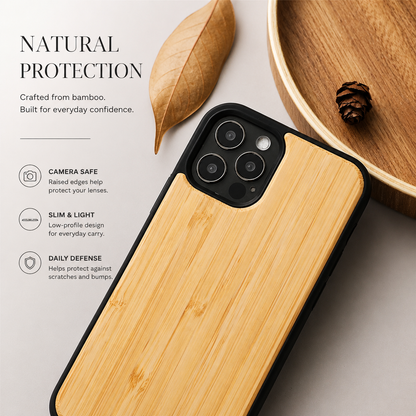 A close-up shows a golden wood-backed phone case lying diagonally on a pale surface beside a dry tan leaf and part of a wooden tray containing a small cone. Three cameras occupy the black surround at the upper left. Text headed 'Natural Protection' identifies bamboo and lists camera safety, slim design, and daily protection.