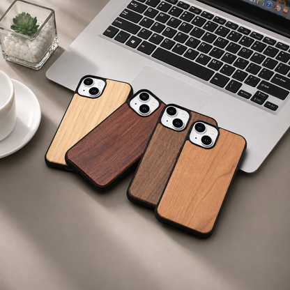 Four wood-backed phones overlap diagonally across the lower edge of a silver laptop on a gray tabletop. The cases have golden, reddish-brown, dark brown, and honey-colored panels, black borders, and pale camera surrounds. A small succulent in a square glass pot sits near the upper left, with a partly cropped white cup and saucer below.