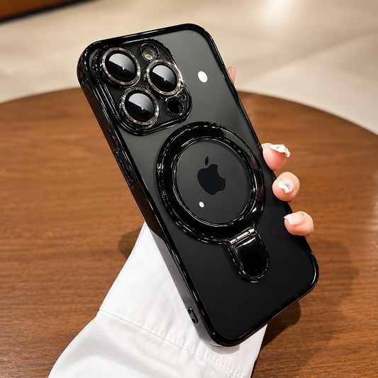 A hand in a white sleeve holds a glossy black clear-backed case above a wooden table. Reflective camera borders and a circular rear ring frame the visible Apple logo. Ceiling-light reflections dot the back, and the ring is folded flat.