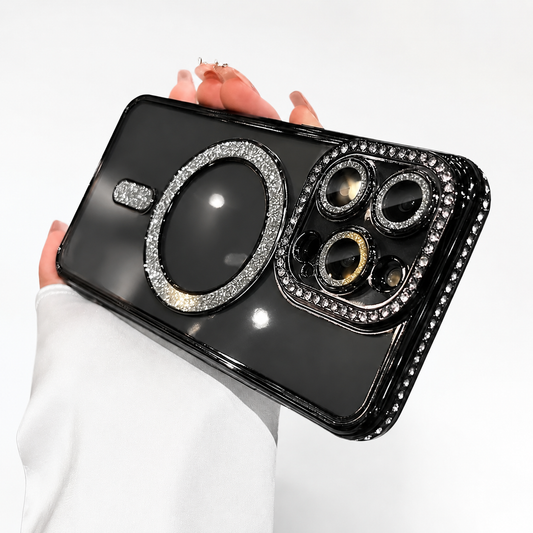 A hand in a white sleeve supports a black phone horizontally against a white background. The glossy back has a large circular ring and short bar covered in small sparkling stones. Three camera lenses sit inside a matching jeweled rectangular surround at the right. Pale manicured fingers curl over the top edge, with a gold-colored ring visible.