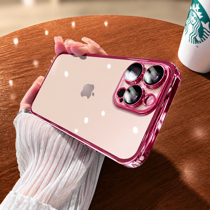 Hand holds a clear pink-edged case horizontally above a wooden table. The pale phone and logo show through its back beneath bright circular reflections.