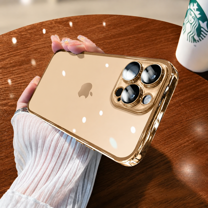 Hand holds a clear gold-colored case horizontally above a wooden table, with reflective camera surrounds and bright circular reflections across the transparent back.