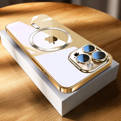 A gold-edged phone rests diagonally on a white rectangular box on a sunlit wooden tabletop. Its pale reflective back shows a circular gold-toned ring around the phone logo and a short bar above. Three camera lenses with blue reflections sit within a gold-colored surround at the nearest end.