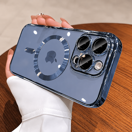 A hand in a white sleeve holds a glossy blue-tinted clear phone case horizontally above a wooden table. A reflective circular magnetic marking surrounds the visible Apple logo, with a short alignment bar below. Reflective raised borders outline the three camera lenses. Small ceiling-light reflections dot the back.
