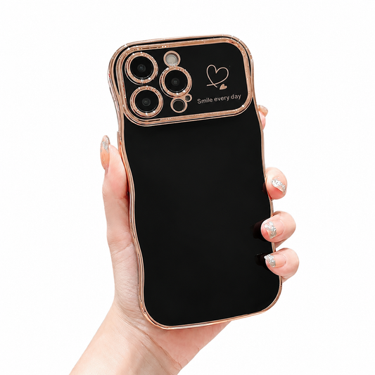 A hand holds a glossy black phone case with wavy rose-gold-colored edging and a camera panel decorated with a heart and 'Smile every day'.