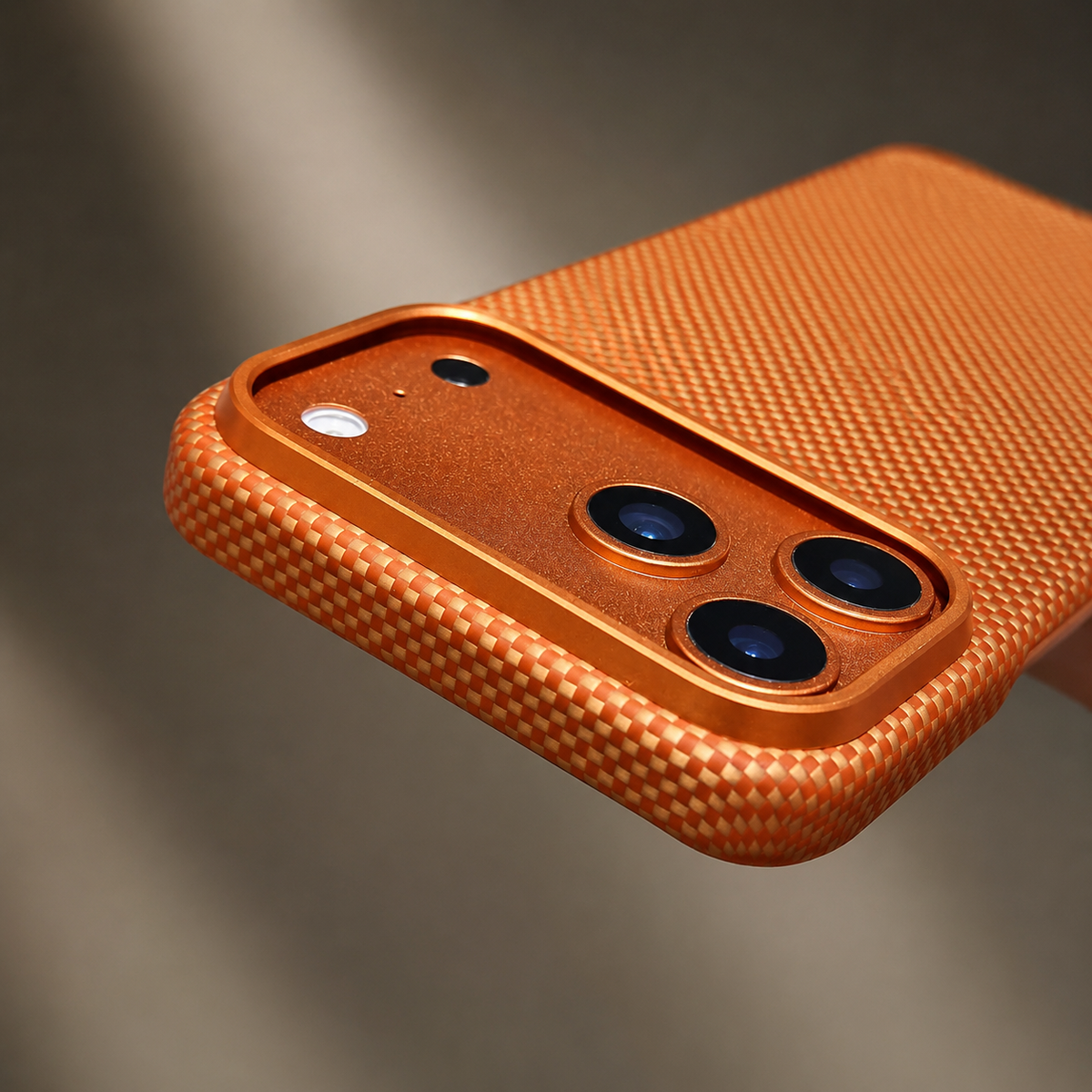 Extreme angled close-up shows the orange woven back and broad camera panel with raised gold border. The rounded case rim casts a soft shadow against gray.