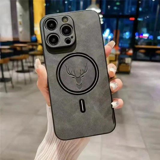 A hand in a pale sleeve holds a gray mottled leather-look phone case upright in a café. An embossed deer head sits inside a black circular ring, with a short black bar below and matching camera trim.