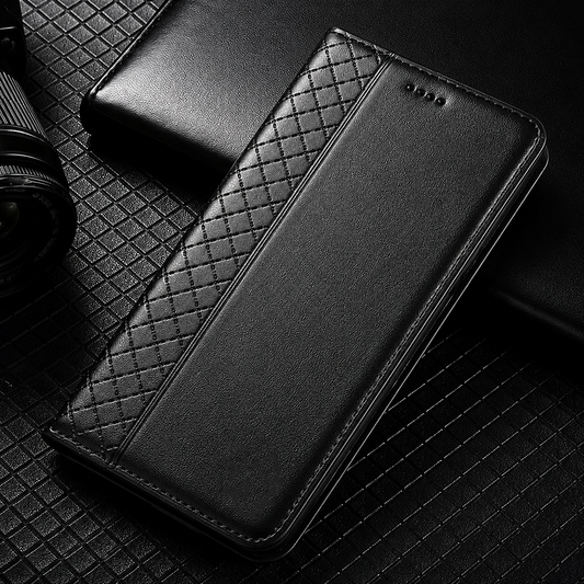 A closed black flip-wallet case lies on a dark patterned desk beside a notebook. A narrow diamond-quilted strip contrasts with its smooth front panel.