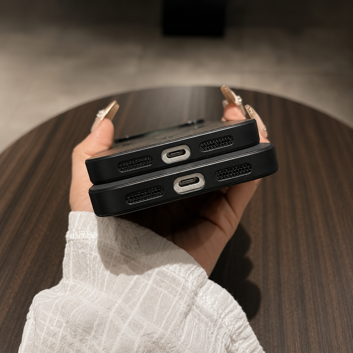 Bottom-edge view of two stacked phones in black cases, with centered charging-port openings and speaker grilles on either side.