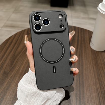 A hand holds a charcoal leather-look phone case above a round wooden table, with a raised camera panel and black circular back ring.