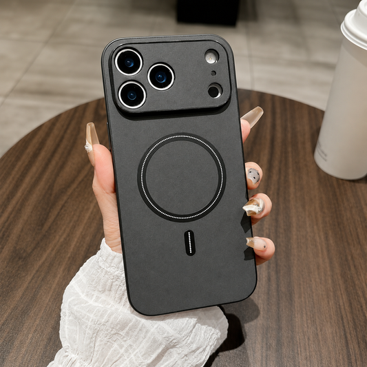 A hand holds a charcoal leather-look phone case above a round wooden table, with a raised camera panel and black circular back ring.