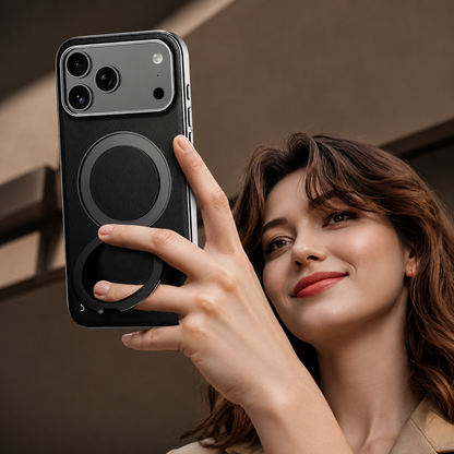 A smiling person holds a black-cased phone above face level, gripping around its circular back ring as though taking a selfie.