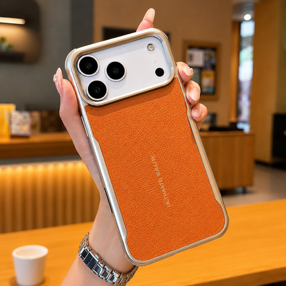 A hand holds an orange leather-look phone case with reflective edging and small gold lettering above a café counter.