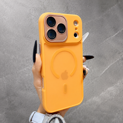 A hand wearing a jeweled watch holds an orange frosted phone case upright against gray stone. An orange ring surrounds the faint Apple logo below a copper-colored three-camera panel.