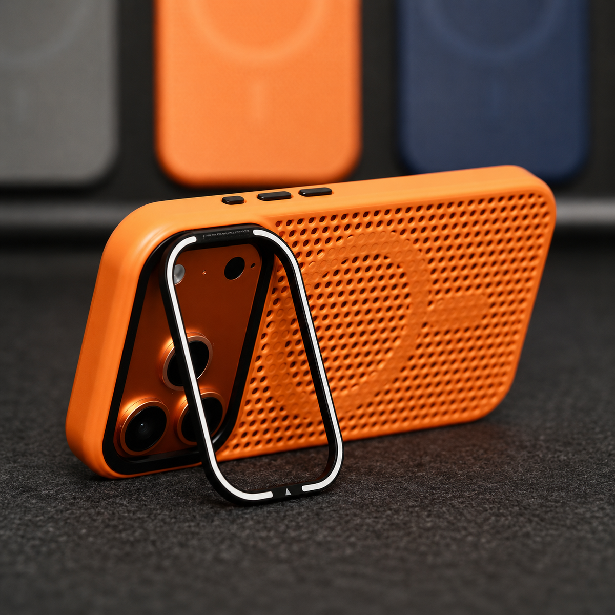 An orange perforated phone case stands horizontally on a silver-edged rectangular camera-frame stand. A solid circular ring and short bar interrupt its mesh-like back.