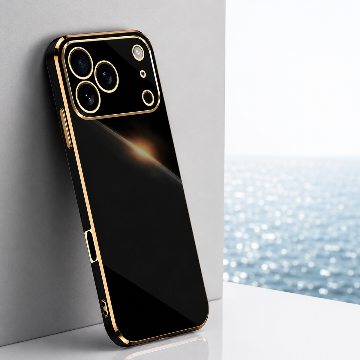 Black glossy phone case with gold-colored trim leaning against a pale block beside a bright window with water visible outside.