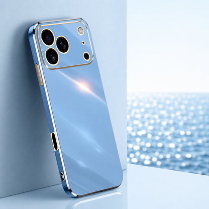 Light blue glossy phone case with gold-colored trim around its edges and camera panel, leaning beside a bright window overlooking water.
