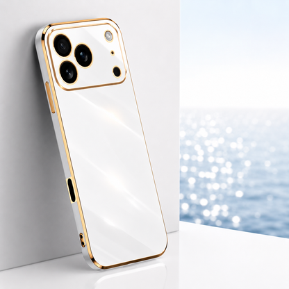 White glossy phone case with gold-colored trim and circular camera outlines, leaning against a pale block beside a bright window.