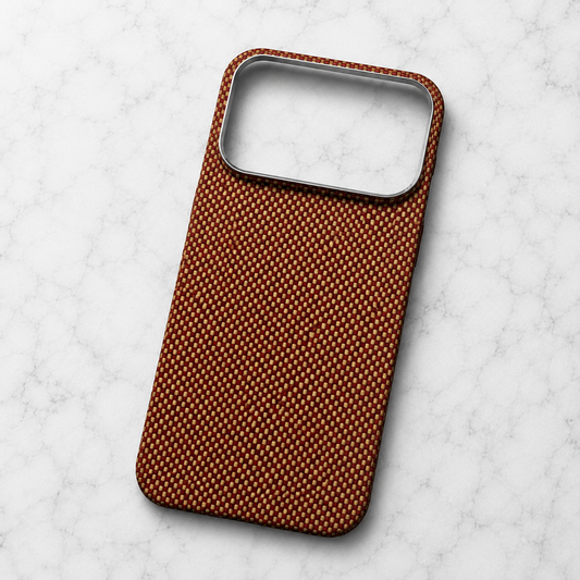 A brown fine-woven phone case lies diagonally on a pale marble-patterned surface, showing a wide rectangular camera opening with silver-colored trim.