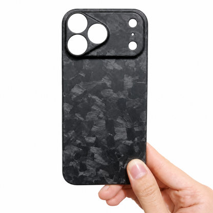 A hand holds a matte black case against white. Irregular gray shard-like patches cover the back, and individual circular openings sit within a broad raised camera panel.