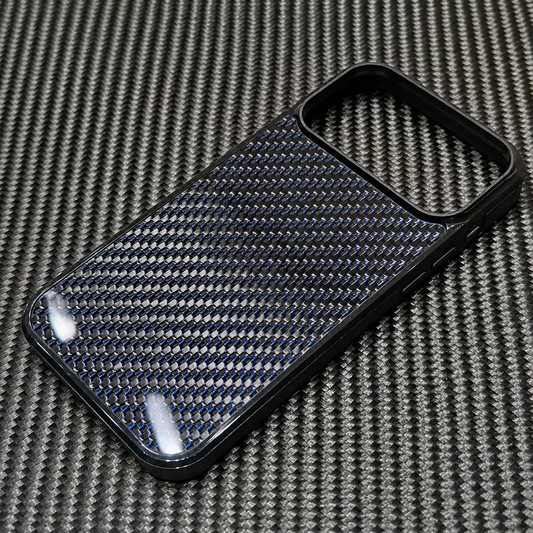 An empty phone case lies diagonally on a larger black-and-gray woven surface. Its glossy back has a regular weave pattern threaded with blue accents inside a smooth black border. A large rounded rectangular camera opening sits at the upper end, with bright white reflections on the lower panel.