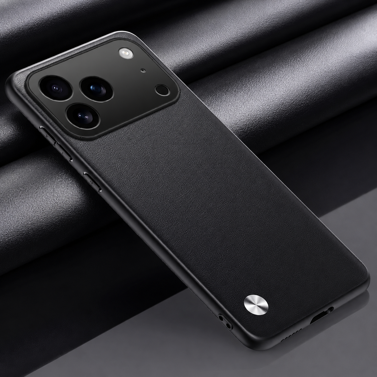 Black textured phone case lying diagonally on dark folded fabric, with a wide camera opening and small silver circular accent at the lower left.